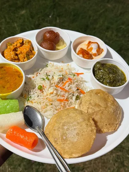 A complete, pure vegetarian meal plated to show you the variety I offer. This particular thali is a Jain meal, featuring vegetable pulao, soft puris, dal, paneer sabzi, and gulab jamun, all prepared without onion or garlic.