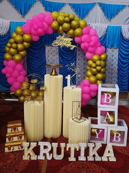 A vibrant pink and gold balloon ring setup against a traditional blue draped tent, creating a festive look for a birthday party.