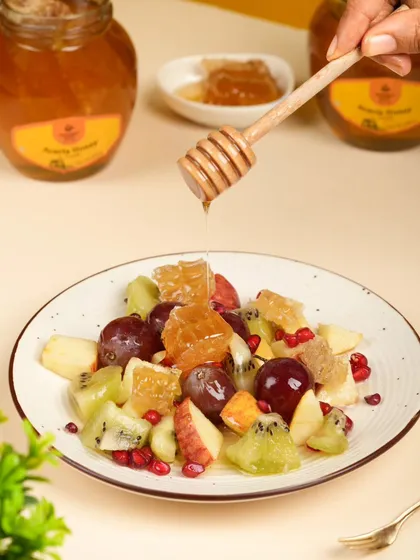 A lifestyle action shot of honey being drizzled over a fresh fruit salad. This image is dynamic and communicates a healthy, delicious way to use the product.