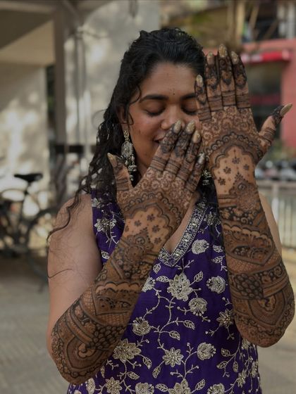 A happy bride showing off her full-sleeve custom mehendi. The joy on her face makes the hours of detailed work completely worth it.