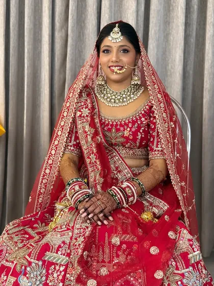 A full-length view of the bride seated, showcasing her magnificent red lehenga and the complete bridal look.