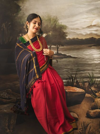 A painterly portrait of a mom-to-be in a red saree, seated by a painted river at dusk, creating a moody and artistic image.