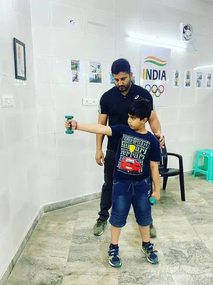 Correcting the posture of a young shooter during a dumbbell holding exercise. This drill builds the specific shoulder and arm muscles needed for competitive pistol shooting.