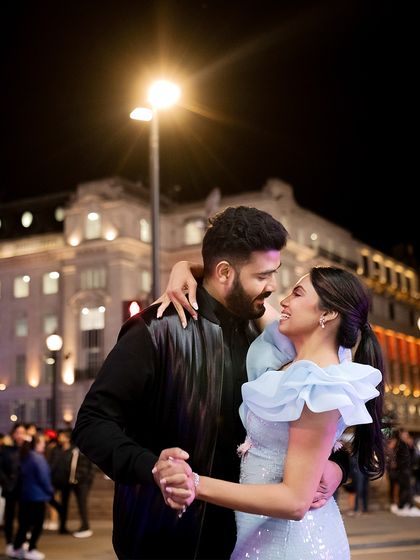 Dancing on the streets of London at night. Her powder blue dress with ruffled shoulders and his sleek black jacket create a modern, romantic look for their pre-wedding shoot.