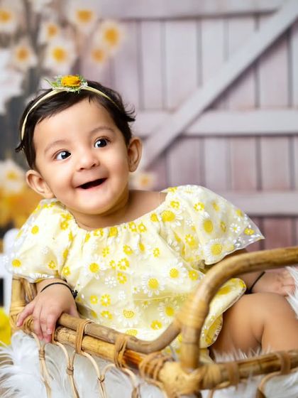 A mischievous and happy grin. This sitter session photo captures the playful personality of a baby girl in a sunny, cheerful floral setting.