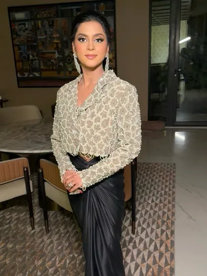 The full look, showing the modern silhouette of the draped skirt and embellished jacket. The makeup is kept elegant and understated to balance the fashion-forward ensemble.