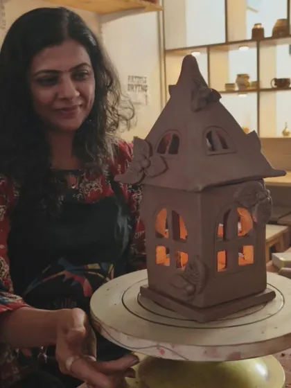 A student admires her handcrafted clay house lantern, lit from within. It is incredibly rewarding to see your creation transform into a functional and beautiful object of art.
