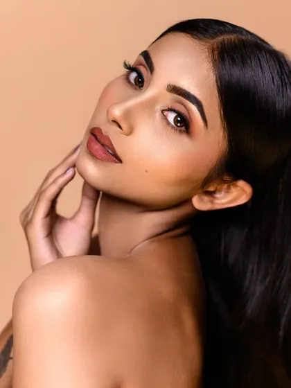 A clean and classic beauty shot against a solid beige backdrop. The lighting is soft and even, perfectly capturing the natural-looking makeup and smooth skin texture.