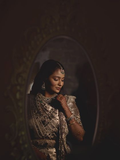 An artistic, moody shot of Sruthi looking into a mirror. The dramatic lighting highlights the contours of her face and the glamour of her makeup.