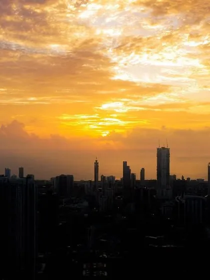 A cluster of clouds catches the golden light of the setting sun, creating a dramatic, fiery sky over a silhouetted Mumbai.