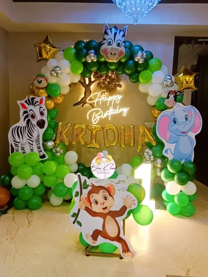 A jungle-themed first birthday with a neon sign, custom backdrop, and character cutouts of a monkey, zebra, and elephant.