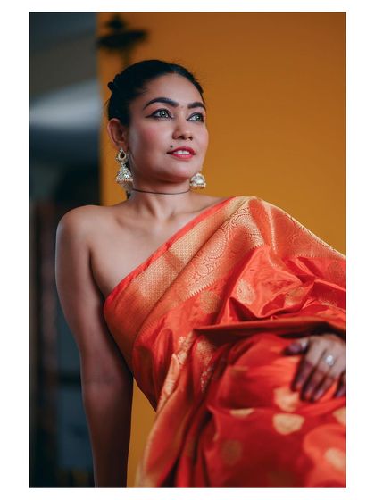 This shot captures the rich texture and color of a silk saree against a warm, solid backdrop. The focus is on the fabric's golden sheen and the model's graceful pose, creating a classic and regal portrait.
