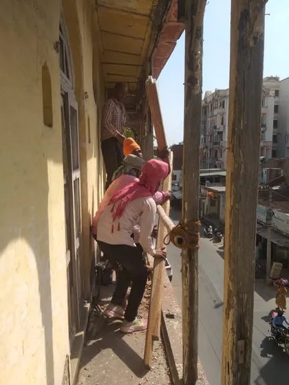 Beginning the meticulous restoration of a 19th-century haveli's facade, with workers carefully removing damaged sections while preserving the structure.