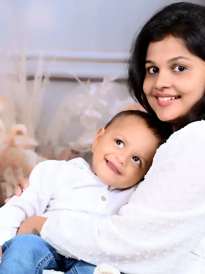 A mother and her baby sharing a happy moment, both dressed in white against a soft, neutral background.