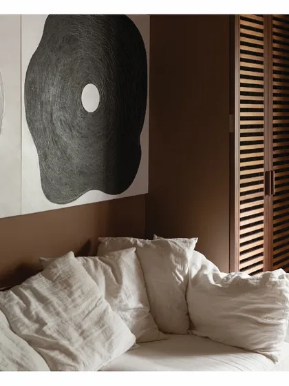 A close-up of the living space in our personal home. A comfortable linen sofa is set against a warm, brown wall, with bold, graphic art creating a focal point. This composition shows how to use deep colors and soft textures to make a compact room feel inviting and rich.
