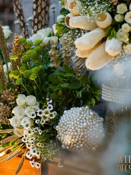 A close-up of a floral arrangement featuring a mix of fresh white roses, green chrysanthemums, and dried wheat stalks, accented by a decorative pearl sphere. This shows a beautiful blend of textures.
