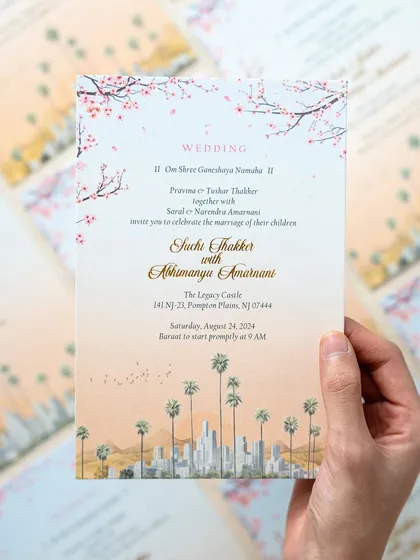A hand holding the main wedding invitation for a Los Angeles ceremony. I illustrated the city's iconic skyline with palm trees in the foreground and cherry blossoms above, blending urban and natural elements beautifully.