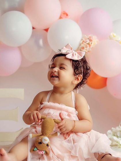 A sweet, cheerful moment from her first birthday portrait session. The soft pinks and whites create a delicate and pretty scene.