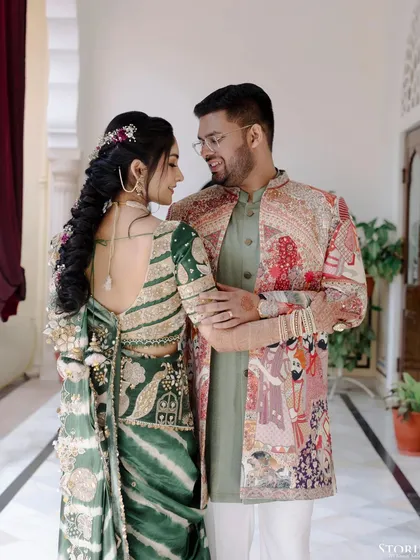 Avi and Anushka looking at each other with love, their traditional outfits standing out against the architectural details of the palace.