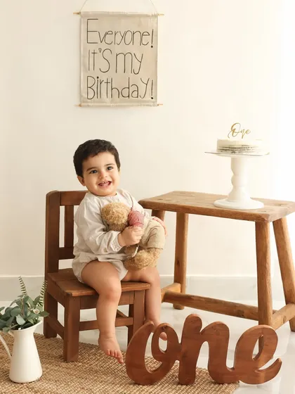 The birthday boy on his throne. This charming portrait with a teddy bear and a birthday banner is a sweet and timeless way to celebrate a first birthday.
