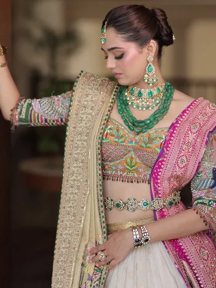 A detailed shot focusing on the intricate embroidery of the blouse and the layered emerald jewellery, highlighting the richness of the look.