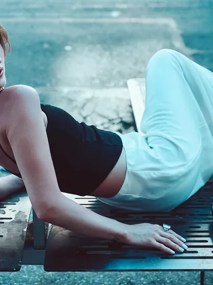 A cool-toned street fashion shot. The blue color grade and the model's relaxed yet poised pose on a metal bench create an edgy, urban vibe.