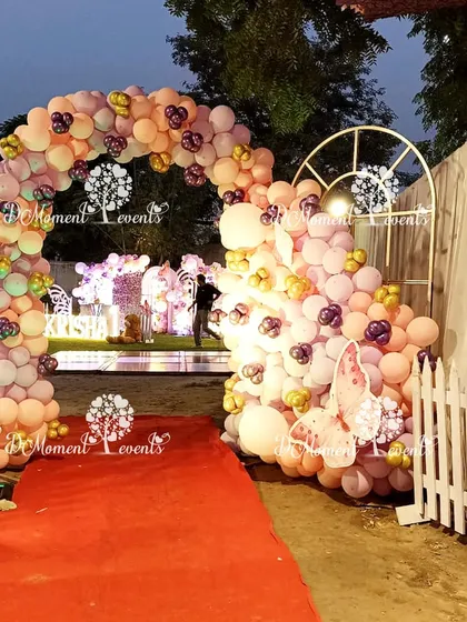 The red carpet entrance to the outdoor butterfly party. A grand balloon arch in peach and purple tones welcomes guests into the enchanting celebration space.