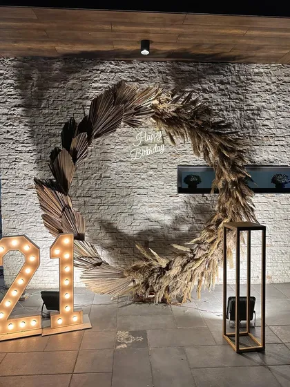 We created this stunning birthday photo backdrop using a large circular frame adorned with dried palm leaves and pampas grass, with a custom neon sign and marquee lights.