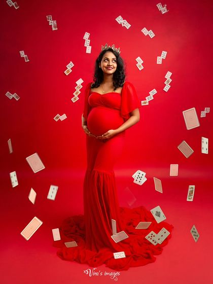 A solo portrait of the "Queen of Hearts," looking up with a hopeful smile as cards rain down around her. A playful and artistic take on the journey to motherhood.