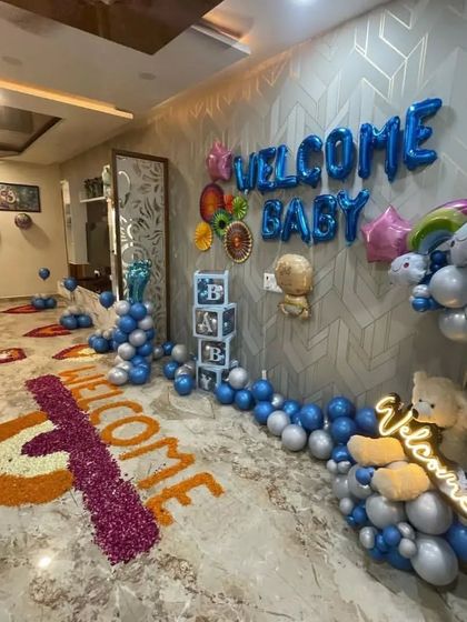 A wide-angle view of the "Welcome Baby" room decoration, showing the flower petal art on the floor and the full balloon setup.