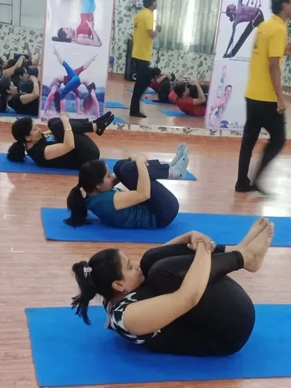 A different angle of the group practicing Pawanmuktasana. The synchronized movement creates a collective energy of focus and release.