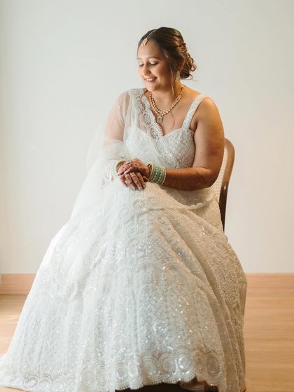 A serene and graceful portrait of a client in a stunning white lehenga. Her makeup is soft and luminous, paired with a classic updo, creating a look of pure elegance for a wedding event.