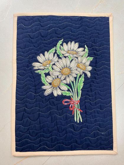 This placemat has an embroidered bouquet of daisies and a wavy quilting pattern.