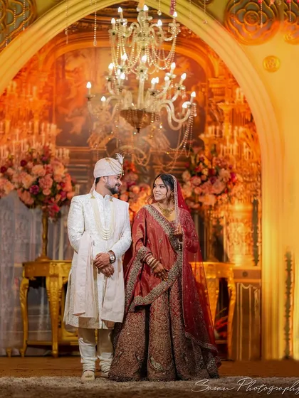 A classic portrait of the bride and groom standing under a magnificent archway in a grand wedding hall.