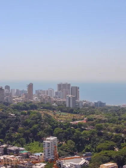 An aerial view of Malabar Hill's lush greenery contrasting with the dense urban development of Mumbai against the sea.