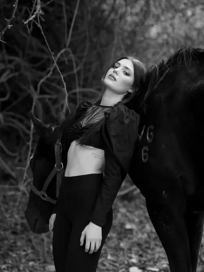 A dramatic black and white shot of a model resting on a horse, showcasing a strong and artistic pose.