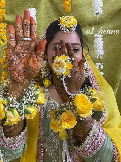 A happy bride Daniya during her mehndi ceremony, showcasing her beautiful henna and floral jewelry. This captures the joy of the moment.