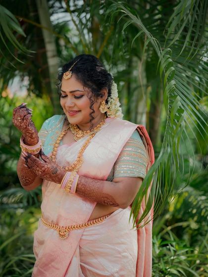 The bride admires the intricate henna on her hands. This candid shot highlights the beauty of her traditional South Indian attire, jewelry, and the happy moments before the ceremony.