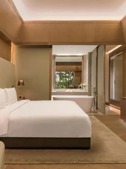 Our rooms are designed to be your personal sanctuary. This suite features a king-sized bed, contemporary furnishings, and a view of the bathroom and greenery beyond.