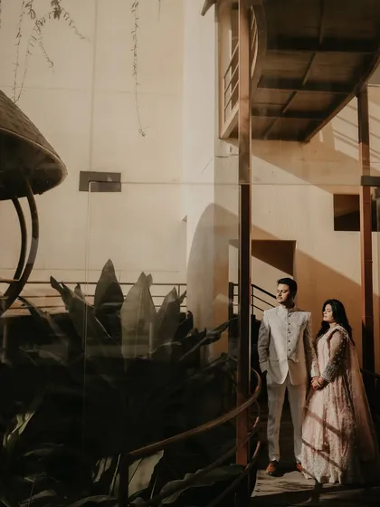 A wide, architectural shot of the couple in a modern setting. The interplay of light, shadow, and structural lines creates a dramatic and stylish pre-wedding portrait.
