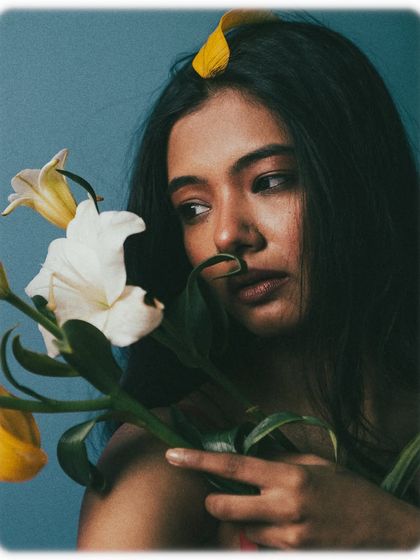 A beautiful, three-quarter portrait where the model interacts with the flower stem. Her expression is thoughtful and distant, adding to the poetic and slightly melancholic mood of the series.