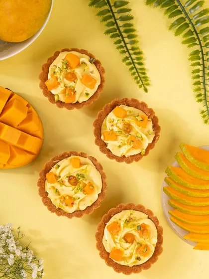 A flatlay of mini mango tarts on a bright yellow background. The composition is playful and summery, perfectly matching the dessert.