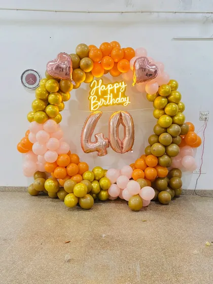A warm and inviting 40th birthday decoration. The circular balloon arch in shades of orange and gold with a neon sign and marquee numbers is perfect for celebrating a milestone.