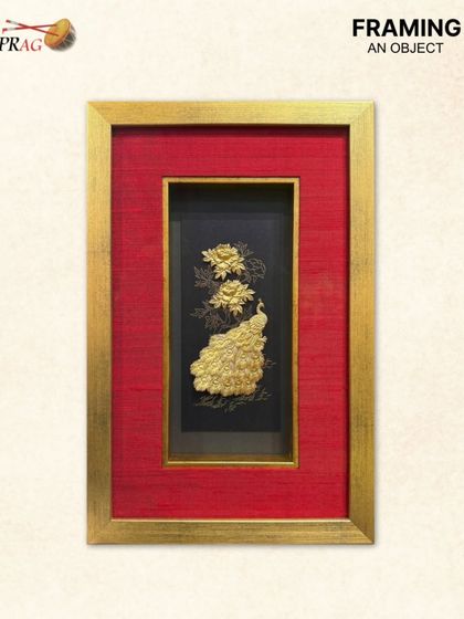 This vertical golden peacock piece showcases intricate floral metalwork alongside the bird. The framing is consistent, using a bold red mount and gold frame to create a cohesive and luxurious look.