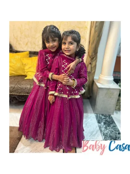 Sisters sharing a hug in their matching magenta ethnic outfits. The intricate gota patti work makes these dresses perfect for a wedding or a grand festive celebration.