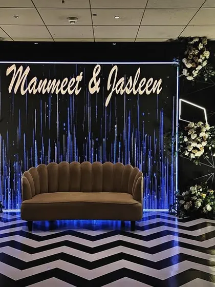 A chic and modern reception stage for Manmeet and Jasleen. The design features a dramatic black and white chevron floor, custom neon-style lighting, and elegant white floral arrangements for a high-impact, contemporary look.