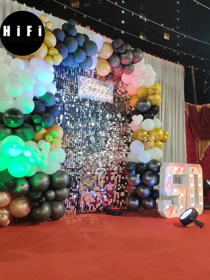 Milestone birthdays deserve a grand celebration. This 50th birthday party decor features a sophisticated black, gold, and silver color scheme with a shimmering sequin wall, a balloon garland, and large marquee numbers to honor the special occasion.