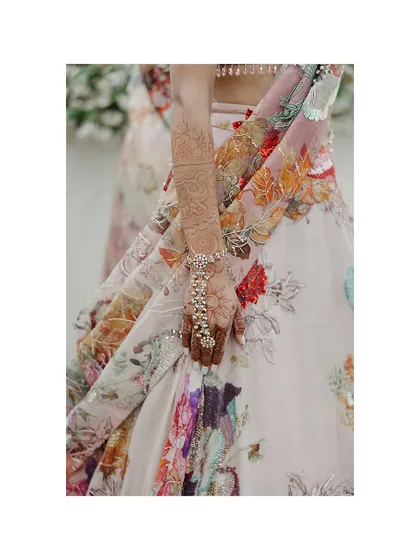 A close-up on the bride's hand, adorned with henna and a beautiful hand harness, resting against the floral print of her lehenga. It's all in the details.