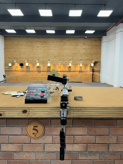 A close-up of a 10M air pistol ready at the firing line. The range is equipped with multiple lanes, each with its own electronic target carrier system for efficient and professional practice.
