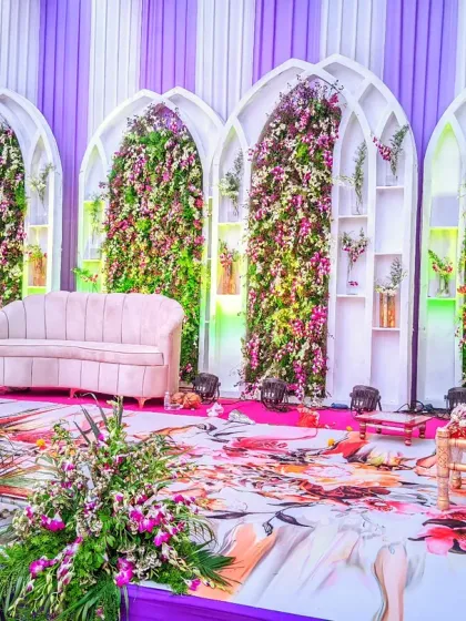 A modern and sophisticated reception stage with a unique backdrop of white arched panels filled with purple and pink flowers, complemented by a stylish lounge sofa for the couple.